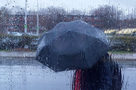 Pedestrian holding an umbrella walking in the rain, with rain drops in the foreground