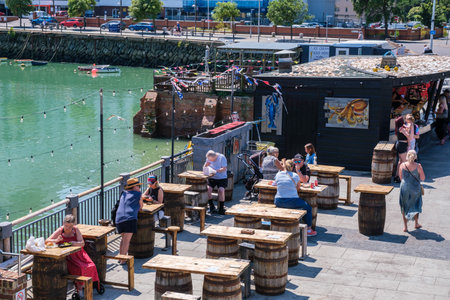 Folkestone, UK - 9 July 2023: People sitting eating fish and chips outside fish and chip shop The...