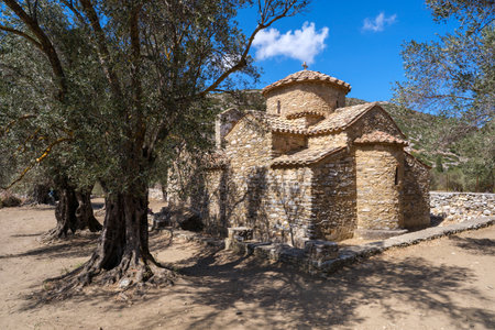The Church of Saint George Diasoritis in Naxos, a small stone church with a red-tiled roof, surrounded by olive trees and hills under a clear blue skyの写真素材