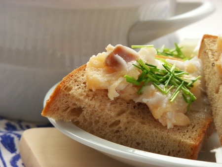 Served lard with cracklings and chives on a slice of fresh bread, all on a white plate and wooden...