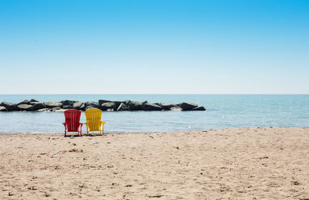 beach scene with yellow and pink adirondack chairs at a sandy city beach with a rock dam in Torontoの写真素材