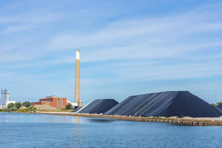 industrial site by a canal or river with storage site covered piles chimneyの写真素材