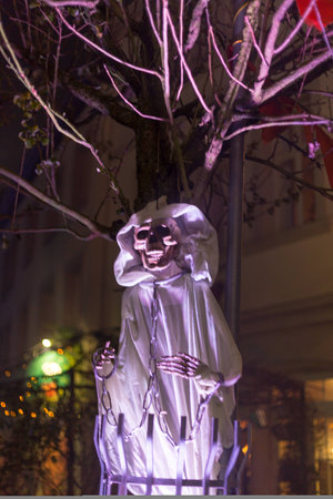 scary sppoky looking skeleton in white cape and hood  with chains as halloween decration in the streets to frighten kidsの写真素材