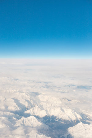 aerial via on the snow capped mountain tops of the alpes and its valleys from airplane blue sky and horizonの写真素材
