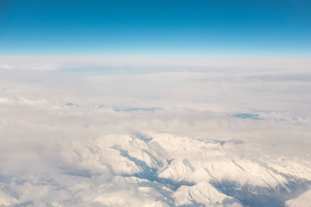 aerial via on the snow capped mountain tops of the alpes and its valleys from airplane blue sky and horizonの写真素材