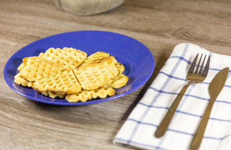 golden heart shaped belgian waffles on blue plate with napkin and cutlery on wooden tableの写真素材