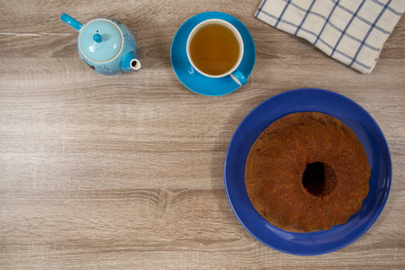 light blue cup and pot of tea with brown cake on deep blue plate on a wooden tableの写真素材