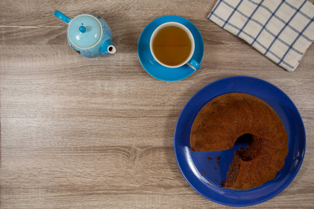 light blue cup and pot of tea with brown cake on deep blue plate on a wooden tableの写真素材