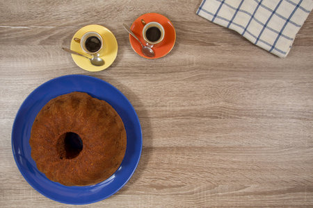 two small espresso in yellow and orange pastel color cups with brown cake on blue plate on wooden tableの写真素材