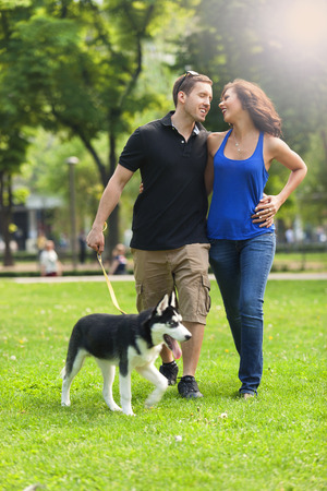 Happy couple in love walking in park with grass with a husky dogの写真素材