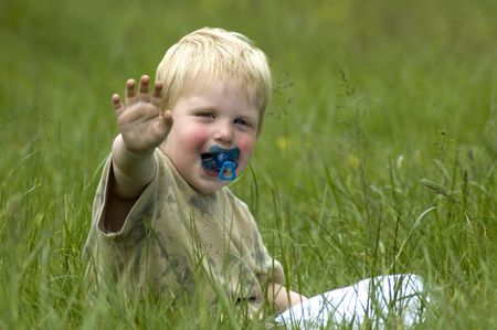 A 2 year old sitting in the grass waving at you.