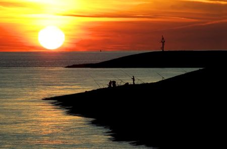 Fisherman at a sea during a beautiful orange and yellow sunset.の写真素材