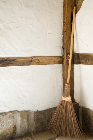 An old wooden straw broom standing against an old wall.の写真素材