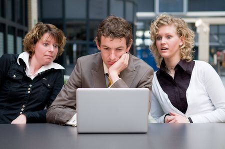 Two businesswoman are shocked by what their male colleague is doing on his laptop...の写真素材