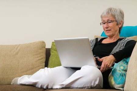 Senior woman working on a laptop, sitting relaxed on the couch.の写真素材