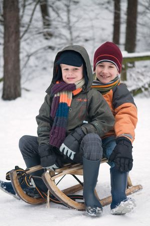 Two young boys sitting on a sled in the snow.の写真素材