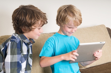 Kid is working on a tablet computer while his brother is watchingの写真素材