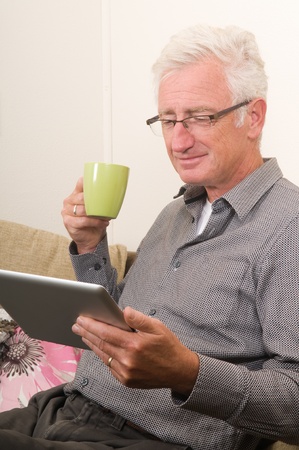 Senior working on a tablet pc while sitting on the couchの写真素材