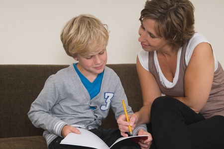 Boy is doing his homework in the livingroom while mother is helping himの写真素材