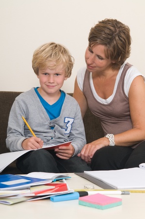 Boy is doing his homework in the livingroom while mother is helping himの写真素材