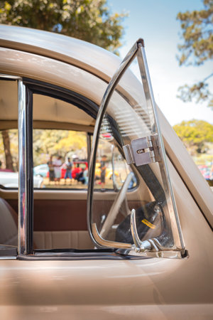 Window of a vintage car with a small pivoting vent window open, highlighting chrome details and a blurred background.の写真素材