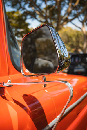 Rear view mirror of a classic vehicle with chrome details, reflecting the surrounding environment with trees in the background.の写真素材