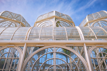 The metallic arch structure, with curved glass panels, forms the central dome of the botanical greenhouse under the blue sky.の写真素材