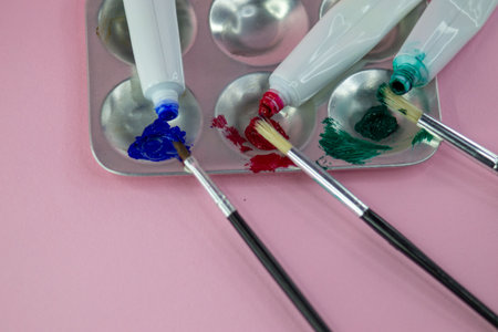 A messy artist's setup features a metal paint palette with six circular wells. Tubes of oil paint in blue, red, and green are squeezed onto the paletteの写真素材