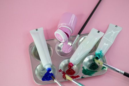 A metal paint palette rests on a pink surface, holding three tubes of oil paint in blue, red, and green, each squeezed to reveal the paint. Nearby, a pink paint bottle is open withの写真素材