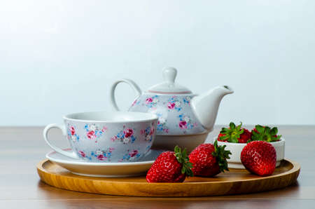 front view of a wooden tray on a table with three strawberries next to a cup of tea, selective focus...
