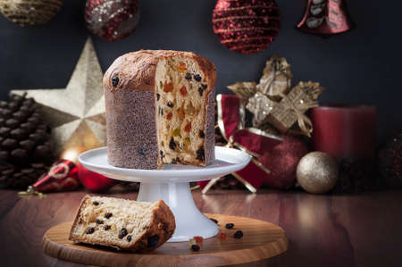 panettone with a slice served on a wooden table with blurred background with christmas decoration.