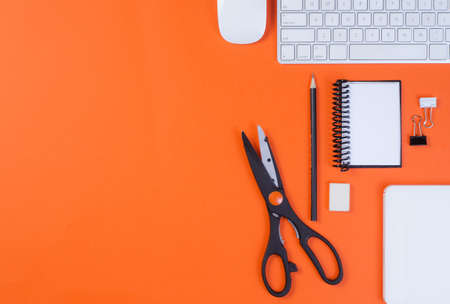 Top view of office work space, orange desk table with keyboard, pencil, scissors, mouse, notebook...
