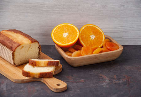 orange cake on a kitchen board with a sliced ââorange and apricot in a wooden bowl, copy spaceの写真素材