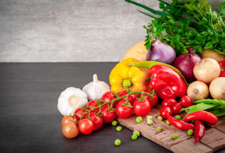 Food background on black wood table. Ingredients for cooking food - cherry tomatoes, onions, potatoes, red and yellow peppers, peas in the pod and garlic. copy space ..の写真素材