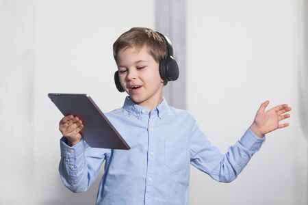 technology - a lovely young pupil rejoicing and jumping with his tablet wearing headphones and...