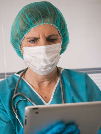 Portrait healthcare professional woman with protection against covid 19 with mask and cap hair using tabletの写真素材