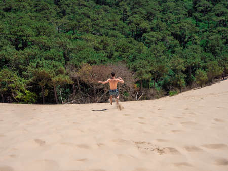 Young caucasian man walking and jumping on the sand in Dune of Pilat in Arcachon Franceの写真素材