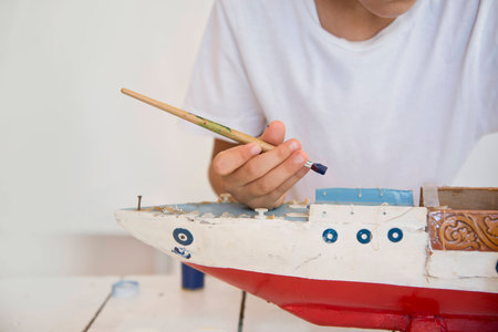 Boy painting old wooden model of a vesselの写真素材