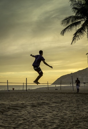 Man practices slack lining at Ipanema Beach in Rio de Janeiro during sunseの写真素材
