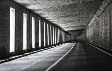 Asphalt road in empty tunnel with turn and lightの写真素材