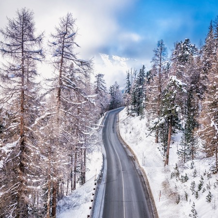 Asphalt curved road leading to high snowy mountains behind fog, winter seasonの写真素材