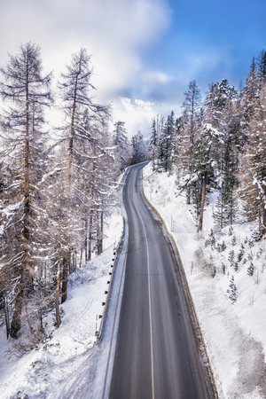 Asphalt curved road leading to high snowy mountains behind fog, winter seasonの写真素材