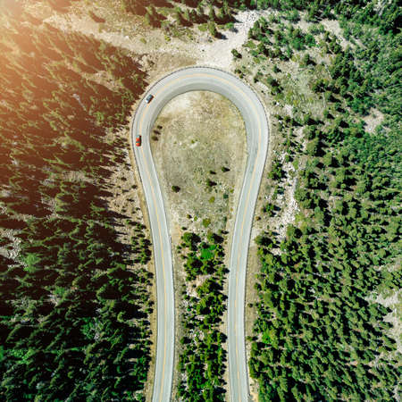 Aerial top down view of cars on curve high mountain asphalt road among green trees, sunny day. Light effect appliedの写真素材