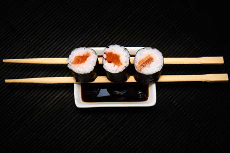 Three pieces of syake maki roll lying on sticks on a black backgroundの写真素材