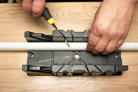 A man cuts a polystyrene baseboard with a clerical knife using a box to cut corners. Renovation...