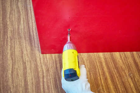 Screwing a screw into a board with a cordless screwdriver, assembling furniture, DIY repair