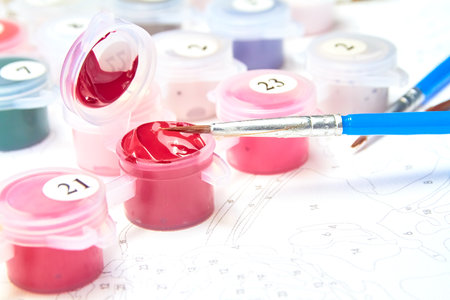 Open jars of watercolor paint and brushes for painting by numbers on the background of a canvas with numbers.の写真素材