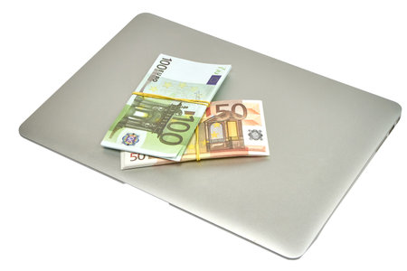 On the computer are stacks of bills of 100 and 50 euros on a white backgroundの写真素材