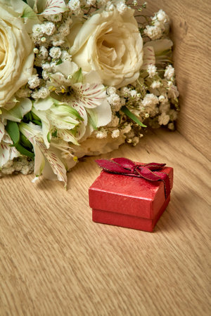 Red gift box with bow on lid, bouquet of white flowers on wooden background, holiday. Vertical orientation of the photo.の写真素材