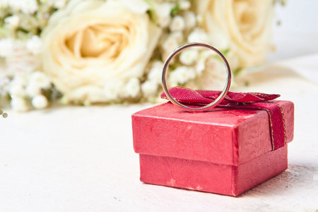 A silver ring stands on a red gift box and a bouquet of flowers on a white textured tree background, holiday.の写真素材